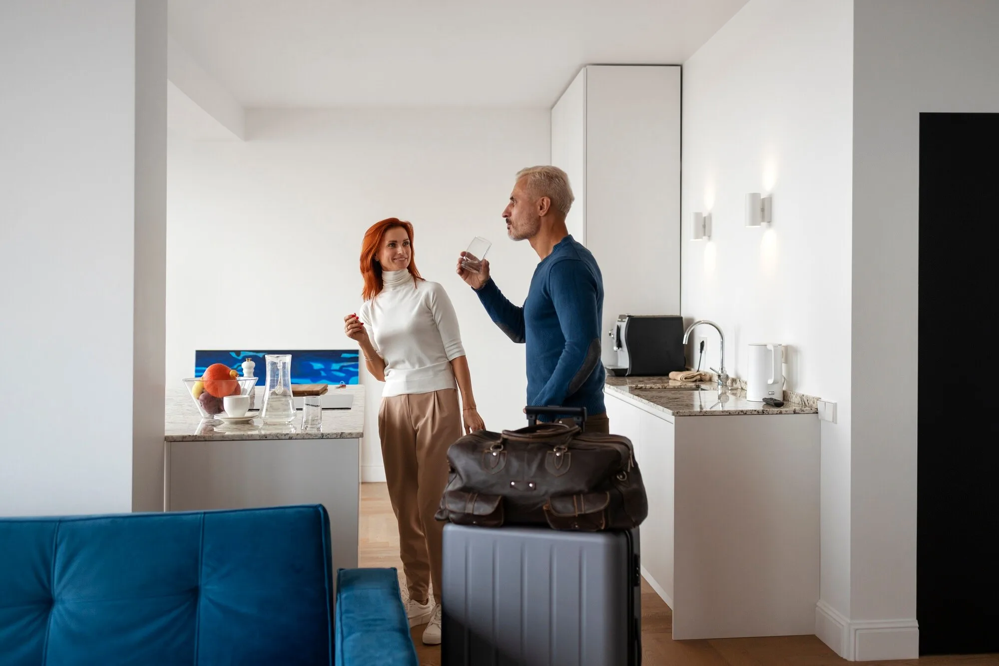 Pareja con maletas bebiendo agua en la cocina